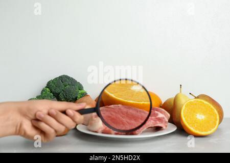 Donna con lente d'ingrandimento che esplora la carne cruda e la frutta, spazio per il testo. Rilevamento di veleni Foto Stock