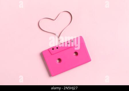 Cassetta musicale e cuore realizzati con nastro su sfondo rosa, vista dall'alto. Ascoltare la canzone d'amore Foto Stock