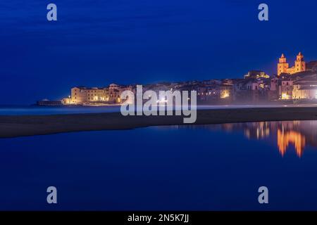 Il pittoresco villaggio balneare di Cefalù si riflette sull'acqua di notte, in Sicilia Foto Stock