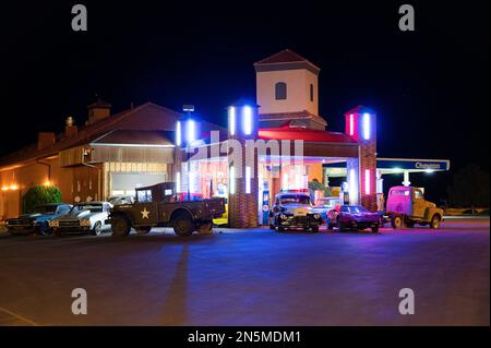 Un vecchio distributore di benzina a bordo strada con auto d'epoca di notte Foto Stock