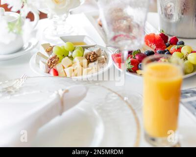 Tavolo servito per banchetti. Piatti con frutta e antipasti, bicchieri da vino trasparenti e moderni e posate su un panno da tavolo bianco. Foto Stock