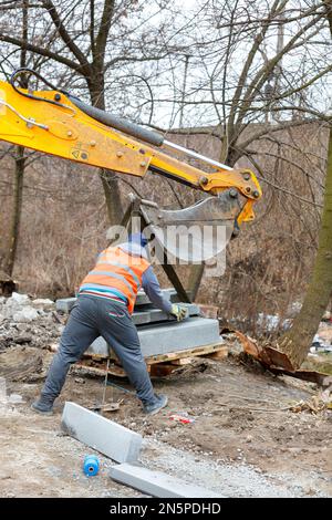 Un lavoratore installa un pallet con lastre di pavimentazione in un luogo di lavoro di costruzione stradale in un giorno di autunno. Foto Stock