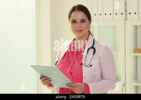 Giovane medico amichevole tenendo appunti con documenti medici, penna e guardando la fotocamera. Foto Stock