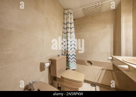 Bagno tradizionale con piano in marmo, specchio senza cornice incastonato in marmo crema, vasca da bagno in porcellana marrone con maniglie e doccia bianca e verde Foto Stock