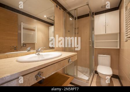 Bagno tradizionale con ripiano in marmo, cabina doccia quadrata con divisori scorrevoli in vetro, grande specchio incassato nella parete e legno bianco ca Foto Stock