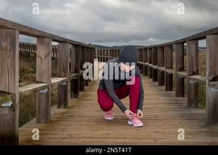 Jogger femminile che lega la sua scarpa, preperazione per una corsa su una passerella di legno Foto Stock