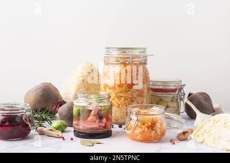 Vasetti di vetro con verdure e ingredienti vari in salamoia su sfondo marmoreo Foto Stock