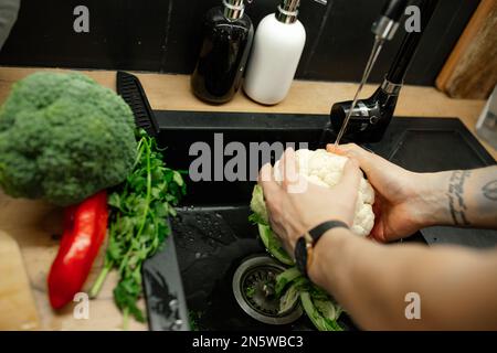 Chiudere le mani dell'uomo irriconoscibili con la pulizia del tatuaggio e lavando cavolo cavolo e pepe verdure in lavatrice Foto Stock