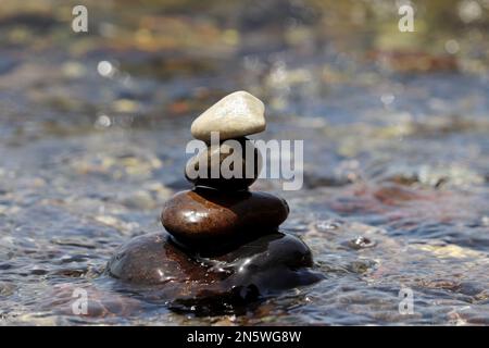 Torre di pietre di ciottoli su sfondo sfocato delle onde del mare. Vacanza in spiaggia, equilibrio e relax concetto Foto Stock