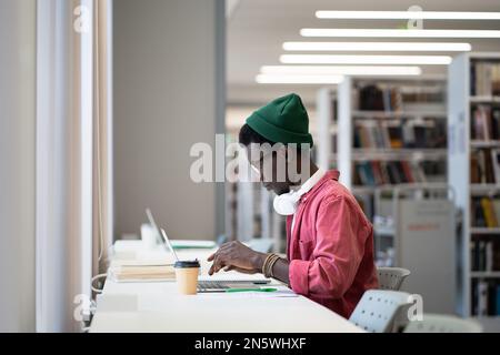 Serio studente uomo prepararsi per l'esame utilizzare il computer portatile per l'istruzione remota presso la biblioteca universitaria Foto Stock