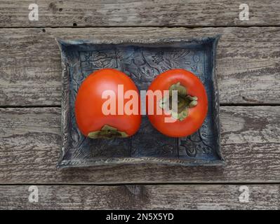 Frutta di persimmon su vassoio di ceramica blu su sfondo di legno, primo piano tavolo vista. Foto dettagliata di frutta kaki con foglia, foto direttamente sopra. Foto Stock