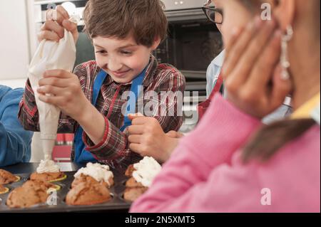 La glassa del ragazzo di scuola sui muffin con il sacchetto della glassa nella lezione domestica di economia, Baviera, Germania Foto Stock