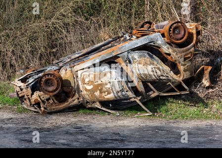 L'auto distrutta si è capovolta sul lato della strada dopo essere stata bruciata in un incidente. Foto Stock