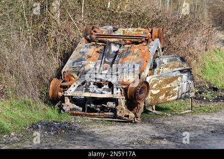 L'auto distrutta si è capovolta sul lato della strada dopo essere stata bruciata in un incidente. Foto Stock