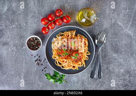 Spaghetti fatti in casa con polpette di salsa di pomodoro e spezie serviti in piatto nero su fondo di cemento grigio. Gustosa pasta cotta con carne di manzo tritata Foto Stock