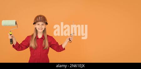 bambino adolescente felice in elmetto costruttore con rullo di vernice e spatola sul muro arancione Foto Stock