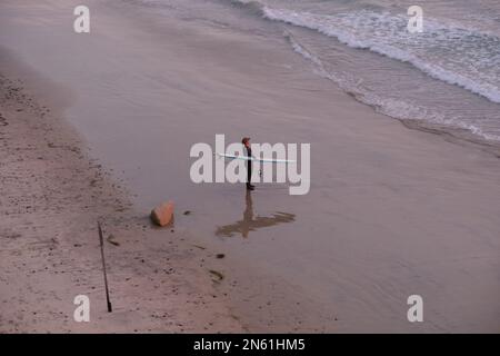 Surfista con bordo in spiaggia Foto Stock