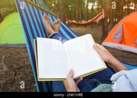 Donna con libro riposante in amaca confortevole all'aperto, primo piano Foto Stock