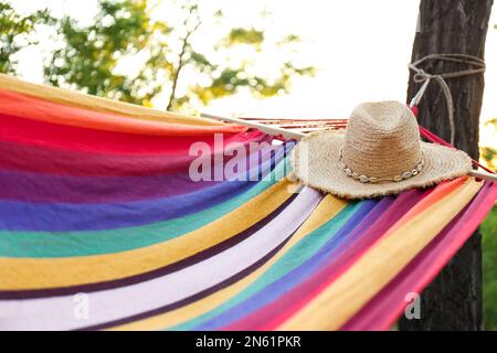 Amaca luminosa e confortevole con cappello in vimini al giardino verde, primo piano Foto Stock