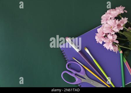 Cancelleria diversa scuola e bellissimi fiori rosa sulla lavagna verde, piatto con spazio per il testo. Buon giorno dell'insegnante Foto Stock