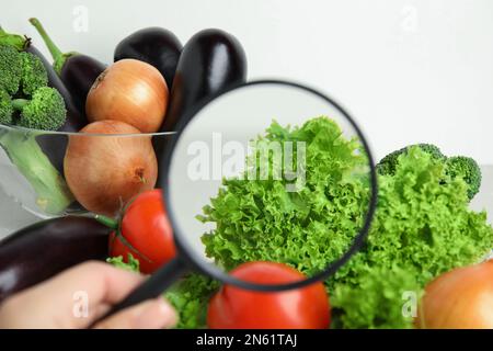 Donna con lente d'ingrandimento che esplora le verdure, primo piano. Rilevamento di veleni Foto Stock