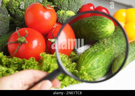 Donna con lente d'ingrandimento che esplora le verdure, primo piano. Rilevamento di veleni Foto Stock