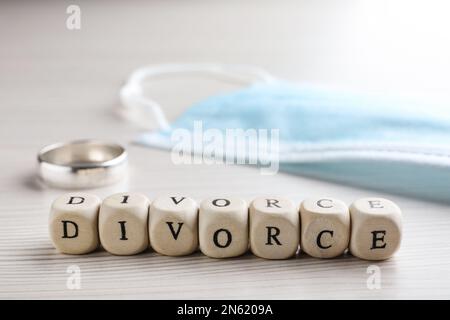 Cubi con parola divorzio, maschera protettiva e anello di nozze su tavolo di legno bianco, primo piano Foto Stock