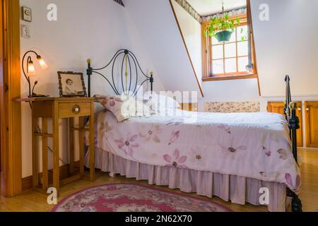 Letto matrimoniale con antico ferro battuto e testiera in ottone e pedana nella camera da letto principale al piano superiore all'interno della vecchia casa del 1927. Foto Stock