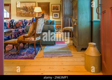 Vecchi armoires in legno, poltrona con cuscino, divano colorato a motivi floreali, poltrona imbottita verde nel soggiorno all'interno della vecchia casa del 1805. Foto Stock