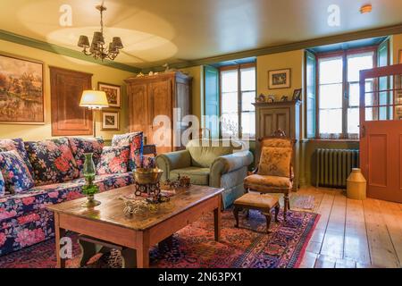 Tavolino da caffè in legno di pino con colorato divano a motivi floreali, poltrona imbottita in verde, poltrona con cuscino e armadio in legno nel soggiorno. Foto Stock