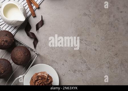 Deliziosi muffin al cioccolato e cupcake decorati con crema su tavolo grigio, piatto. Spazio per il testo Foto Stock