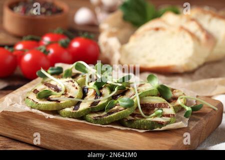 Deliziose fette di zucchine grigliate con microgreens su asse di legno, primo piano Foto Stock