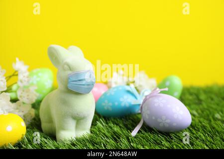 Pandemia COVID-19. Coniglio di Pasqua in maschera protettiva e uova tinte su erba verde Foto Stock