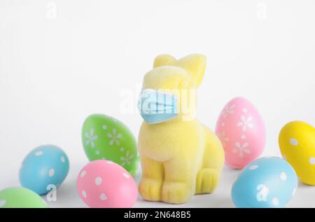 Pandemia COVID-19. Coniglio di Pasqua in maschera protettiva e uova tinte su sfondo bianco Foto Stock