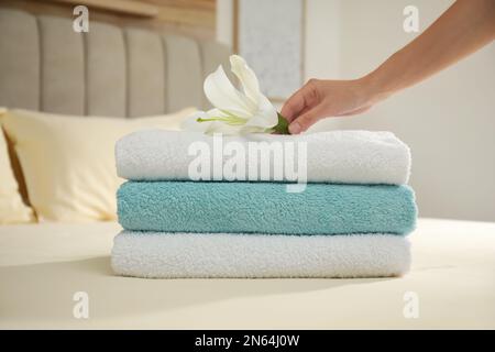Donna che mette fiore su pila di asciugamani puliti in camera da letto, primo piano Foto Stock