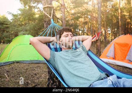 Uomo che dorme in una comoda amaca vicino alle tende all'aperto Foto Stock