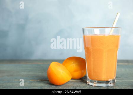 Gustoso frullato al persimmon con paglia e frutta fresca su un tavolo di legno su sfondo azzurro. Spazio per il testo Foto Stock