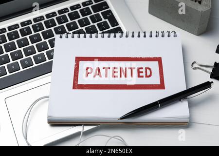 Notebook con francobollo BREVETTATO su tavolo di legno bianco, primo piano Foto Stock