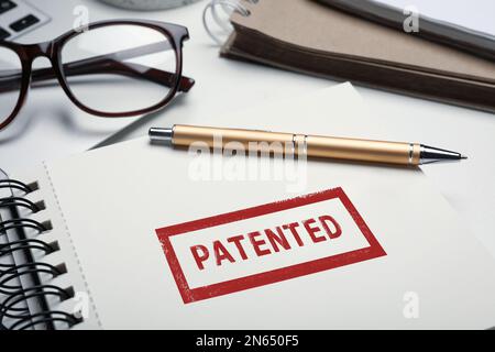 Notebook con francobollo BREVETTATO e penna su tavolo, primo piano Foto Stock