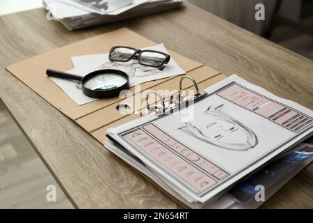 Carte con ritratto di sospetto, stampa palmo e lente d'ingrandimento su tavolo di legno in ufficio detective Foto Stock