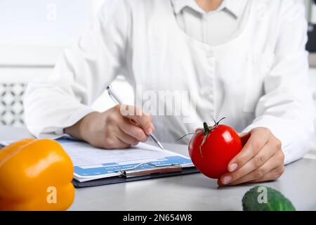 Scienziato con forma di prova di laboratorio e pomodoro fresco a tavola all'interno, primo piano. Rilevamento di veleni Foto Stock