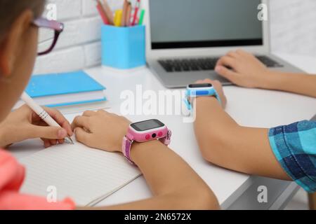 Bambini con eleganti orologi intelligenti al tavolo bianco, primo piano Foto Stock