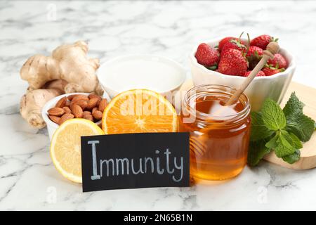 Scheda con parola immunità e prodotti freschi su sfondo marmo chiaro Foto Stock