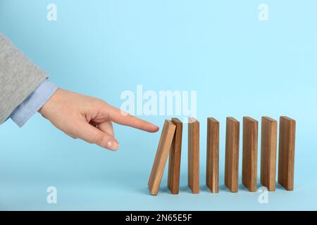 Donna che causa la reazione a catena spingendo la tessera domino su sfondo azzurro, primo piano Foto Stock