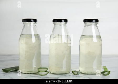 Bevanda fresca all'aloe in bottiglia e fettine di foglie su un tavolo di marmo bianco Foto Stock