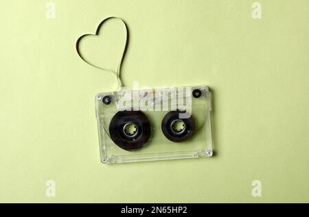 Cassetta musicale e cuore realizzati con nastro su sfondo verde, vista dall'alto. Ascoltare la canzone d'amore Foto Stock