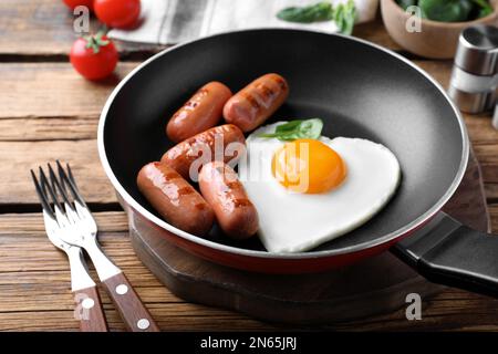 Colazione romantica con salsicce fritte e uovo a forma di cuore su tavolo di legno. Festa di San Valentino Foto Stock