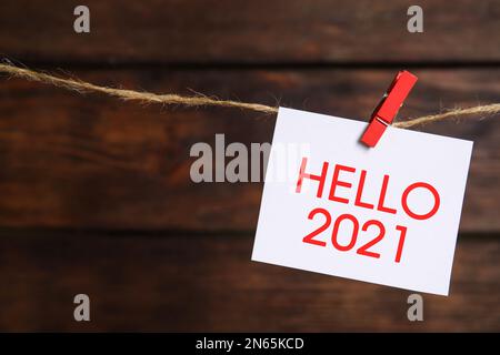 Nota cartacea con frase Hello 2021 appeso a spago su sfondo di legno, spazio per il testo Foto Stock