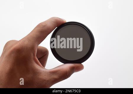 La mano dell'uomo tiene un filtro ottico ND (a densità neutra) isolato su sfondo bianco Foto Stock