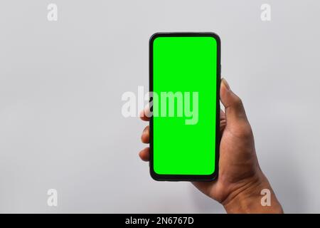 Simulazione di dispositivi mobili. Mano dell'uomo che tiene lo smartphone nero con schermo verde in posizione verticale isolato su sfondo bianco. Foto Stock